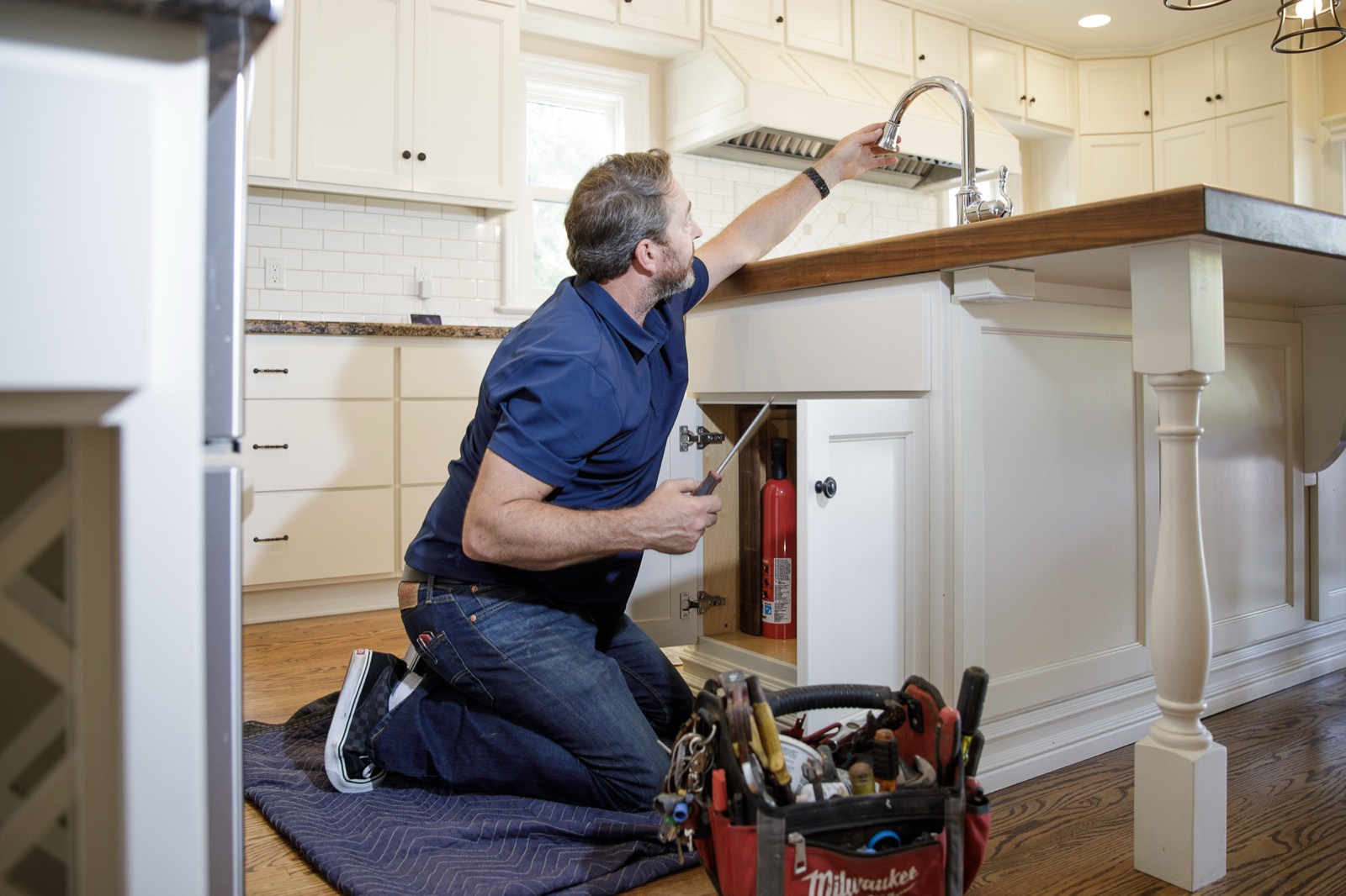 Joe installing a new kitchen faucet under a farmhouse-style island sink